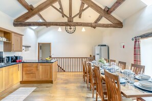A dining area with wooden chairs and a table set for six, a kitchen with wooden cabinets, and a high ceiling with exposed beams. - 5 Bed in Litton (oc-l31793) (Litton)
