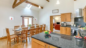 Una cocina amplia con vigas de madera, una zona de comedor con sillas de madera y una encimera con un frutero.