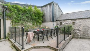 Un patio con una mesa y sillas, un muro de piedra y un edificio de madera.
