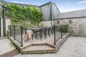 Une terrasse avec une table et des chaises, un mur en pierre et un bâtiment en bois.