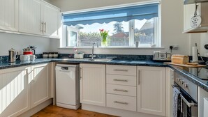 Een moderne keuken met witte kastjes, een vaatwasser, een broodrooster en een raam met uitzicht op een tuin.