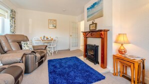 Een woonkamer met een bruine leren bank, een blauw vloerkleed, een open haard en een eethoek met een tafel en stoelen.