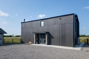 En moderne bygning med mørk facade, murstensindgang og grusvej.