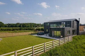 Un bâtiment moderne à deux étages, doté d’un toit plat, de grandes fenêtres et d’un espace extérieur aménagé avec des sièges.