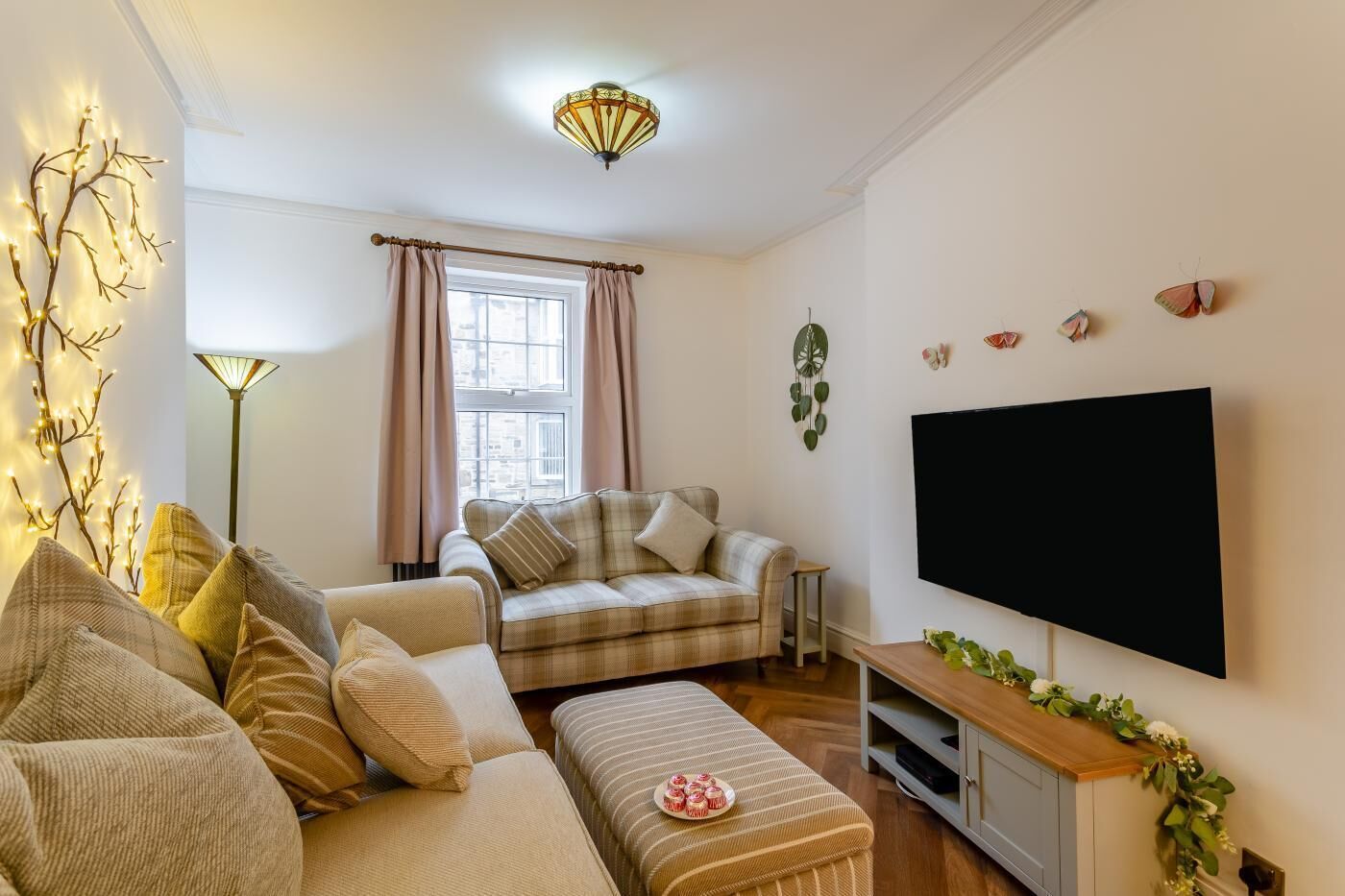 Een gezellige woonkamer met een bank, een poef en een flatscreen televisie op een standaard.