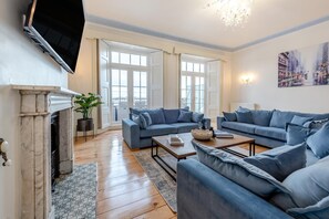 A living room with a fireplace, two sofas, a coffee table, and a large window. - 6 Bed in Tenby (oc-c31800) (Tenby)