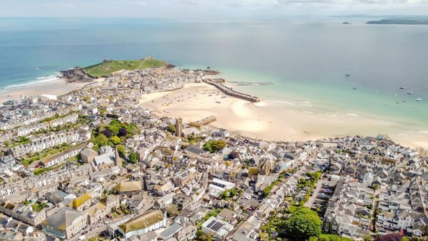 An aerial view of a coastal town with a sandy beach, residential buildings, and a fortified structure on a hill. - 4 Bed in St. Ives (oc-p31118) (Saint Ives)