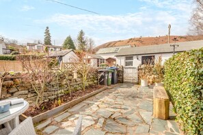 Ein gepflasterter Innenhof mit Steinmauer, einer hölzernen Bank und einem Metallgitter.