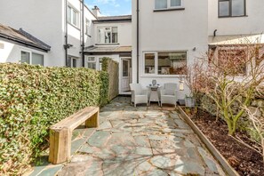 A narrow stone pathway leading to a white door, flanked by a hedge and a wooden bench. - 2 Bed in Braithwaite (oc-p31730) (Braithwaite)