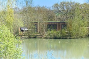 Ein Gebäude am Seeufer mit Holzfassade, umgeben von Bäumen und ruhigem Wasser.