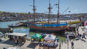 A large sailing ship docked at a harbor with a crowd of people and market stalls nearby. - 2 Bed in Whitby (oc-h31801) (Whitby)