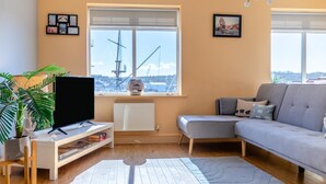 A living room with a TV, sofa, and a large window with a view of a ship. - 2 Bed in Whitby (oc-h31801) (Whitby)
