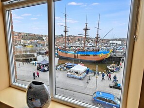 A view of a harbor with a large sailing ship docked, a market area with stalls, and a blue car parked on the street. - 2 Bed in Whitby (oc-h31801) (Whitby)