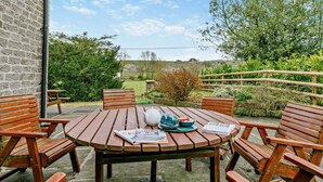 Een ronde houten tafel met vier stoelen, een theepot, kopjes en een krant.