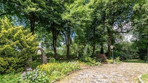 Een geplaveid pad in een weelderige tuin met dichte bomen en een stenen boog.