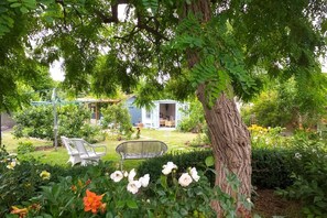 Un jardín con un árbol, una caseta pequeña y dos sillas.