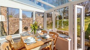 A dining area with a table set for four, large windows, and a stone wall in the background. - 2 Bed in Little Haven (oc-i31766) (Little Haven)