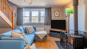 A cozy living room with a blue sofa, a TV, a fireplace, and a staircase. - 2 Bed in Little Haven (oc-i31766) (Little Haven)