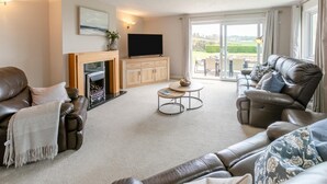 Ein geräumiges Wohnzimmer mit Kamin, Ledersofas, einem Flachbildfernseher und Blick ins Freie.