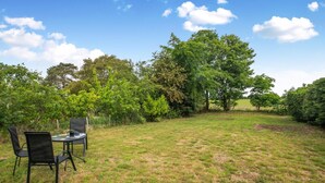An outdoor seating area with a table and chairs, surrounded by a grassy field and trees.