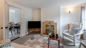 A living room with a television, a fireplace, a coffee table, and a white armchair.