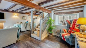 A spacious living area with a staircase, wooden beams, a dining set, and a cozy seating area with a flag-patterned cushion. - 4 Bed in Cartmel (oc-d31802) (Cartmel)