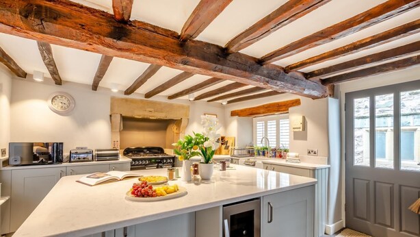 A modern kitchen with a large island, wooden beams on the ceiling, and a view of the outside through a window. - 4 Bed in Cartmel (oc-d31802) (Cartmel)
