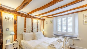 A bedroom with exposed wooden beams, a white bed, bedside lamps, and a window with blinds. - 4 Bed in Cartmel (oc-d31802) (Cartmel)