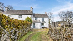 A stone wall with a grassy path leading to a white house with multiple windows and a chimney. - 2 Bed in Windermere (oc-c31666) (Crook)