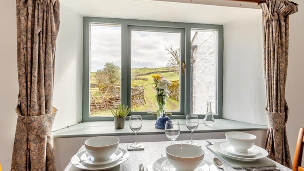 A dining table set for four with a view of a rural landscape through a window. - 2 Bed in Windermere (oc-c31666) (Crook)