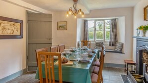 A dining room with a long table set for six, wooden chairs, a chandelier, a fireplace, and a window with curtains. - 3 Bed in Windermere (oc-b31667) (Crook)