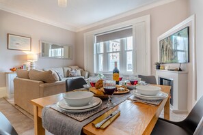 Un coin repas avec une table en bois dressée pour deux personnes, un canapé et une cheminée.