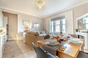 A dining area with a table set for two, a sofa, and a kitchen in the background. - 2 Bed in Whitby (oc-e31738) (Whitby)