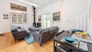 Ein modernes Wohnzimmer mit zwei Sofas, einem Esstisch mit blauer Tischdecke und einer Küchenzeile mit Schränken und einem Herd.
