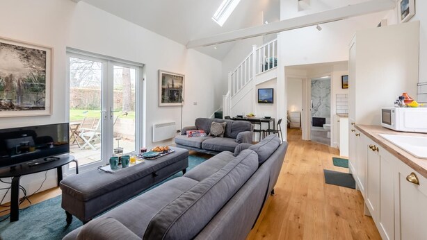 Ein modernes Wohnzimmer mit einem grauen Sofa, einem Fernseher und einem Essbereich mit Tisch und Stühlen.