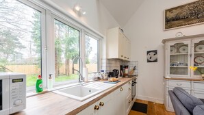 Eine Küche mit großem Fenster, weißen Schränken, einer Mikrowelle und einem Spülbecken.