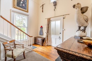 A staircase leading to a landing with a wooden chair, a wooden table with a decorative edge, a wall-mounted clock, and a bird sculpture. - 5 Bed in Battle (oc-c31779) (Battle)