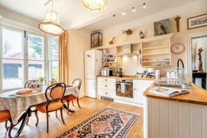 Une cuisine avec un coin repas, des meubles de rangement en bois, un four encastré et une grande fenêtre.
