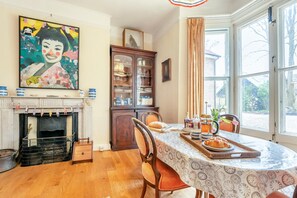 Un coin repas avec une table dressée pour deux personnes, une cheminée, un buffet et une grande fenêtre donnant sur un beau paysage.