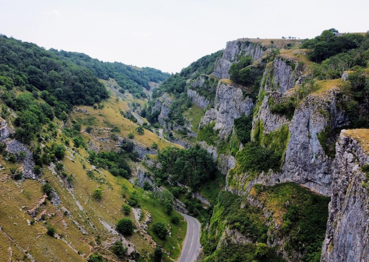 A winding road through a mountainous landscape with rocky cliffs and dense greenery.