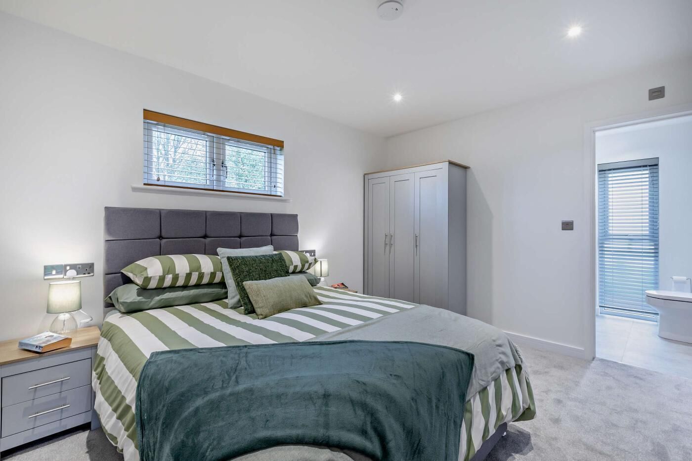 Een slaapkamer met een bed, nachtkastje, lamp, kledingkast en een raam met zonwering.
