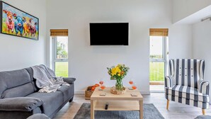 Una sala de estar moderna con un sofá gris, una mesa de centro de madera con bebidas, un sillón a rayas y un televisor en la pared.
