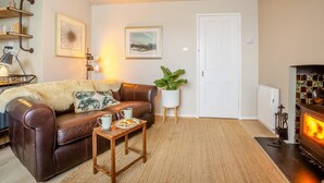 A cozy living room with a brown leather sofa, a small wooden coffee table with a plate of food, a potted plant, and a fireplace. - 1 Bed in Llanfairfechan (oc-t31122) (Llanfairfechan)