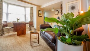 A cozy living room with a leather sofa, a dining table, and a large potted plant. - 1 Bed in Llanfairfechan (oc-t31122) (Llanfairfechan)