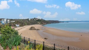 A coastal beach with a sandy shore, a rocky outcrop, and a clear blue sky. - 2 Bed in Tenby (oc-o31794) (Tenby)
