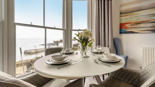 A dining area with a round table set for four, overlooking a coastal view. - 2 Bed in Tenby (oc-o31794) (Tenby)