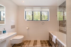 A modern bathroom with a toilet, sink, and bathtub. There is a window providing natural light and a view of trees. - 2 Bed in Windermere (oc-m31843) (Windermere)