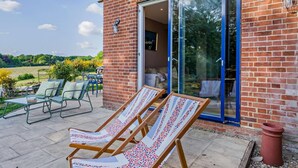 A brick building with a glass door leading to a patio area with outdoor seating and a view of the countryside. - 2 Bed in Holbrook (oc-31111) (Lower Holbrook)