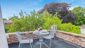Eine Terrassengruppe im Freien mit zwei Metallstühlen und einem runden Tisch, einer Weinflasche und einem Weinglas.
