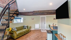 Ein Wohnzimmer mit einem grünen Sofa, einem Holzboden im Fischgrätmuster, einer Wendeltreppe und einem an der Wand befestigten Flachbildfernseher.